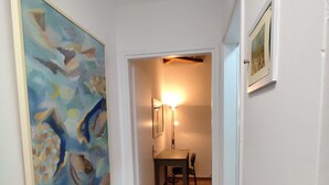 Un couloir avec un sol carrelé, un coin repas avec une table et des chaises, et un tableau accroché au mur.