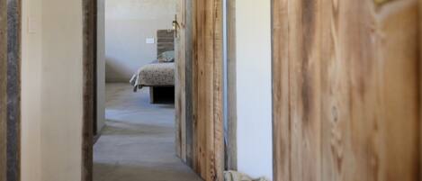 A hallway leading to a bedroom with a bed, a suitcase, and wooden doors.