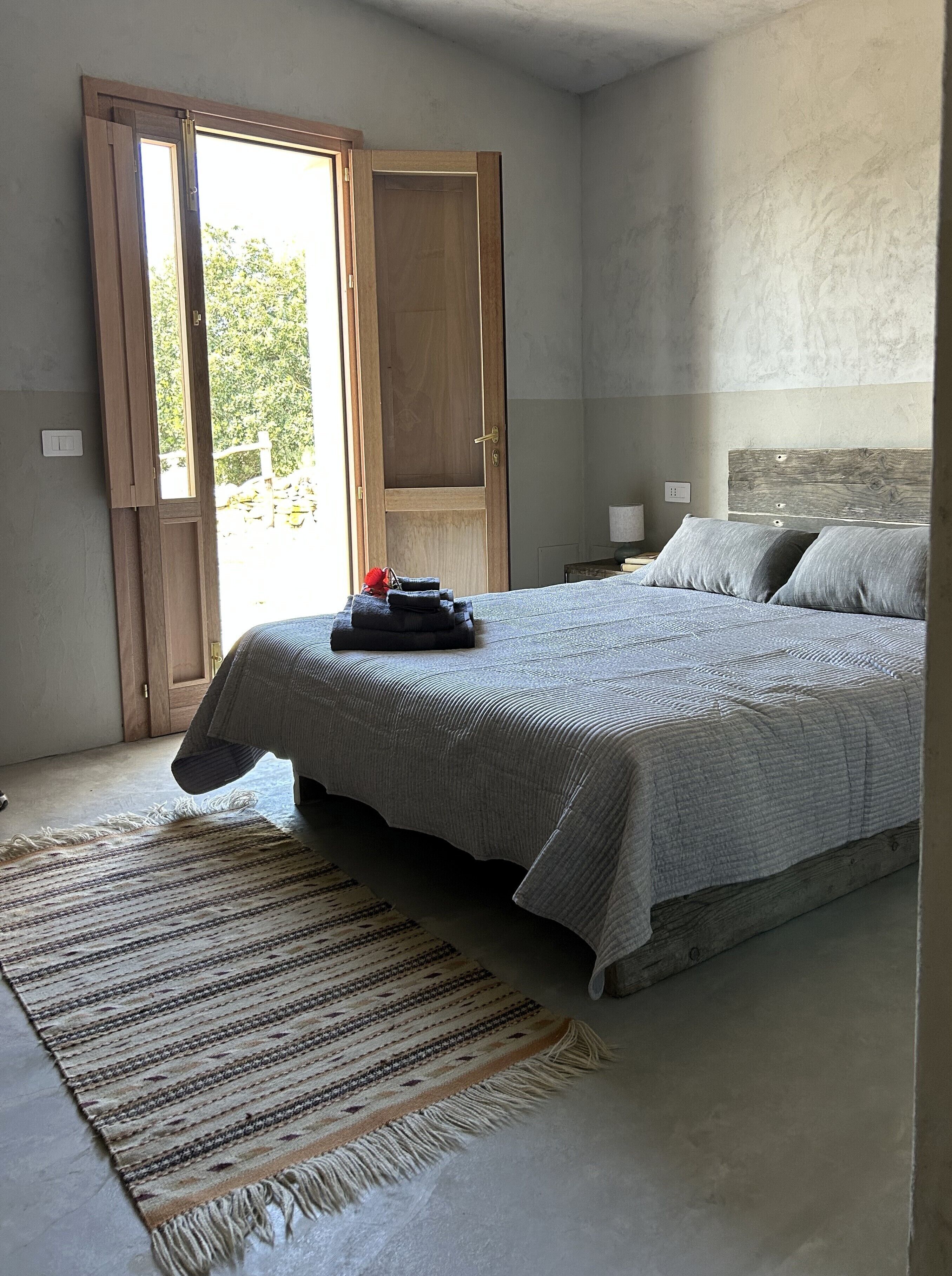 Une chambre à coucher avec un lit, une table de chevet, une porte en bois et une vue sur la verdure.