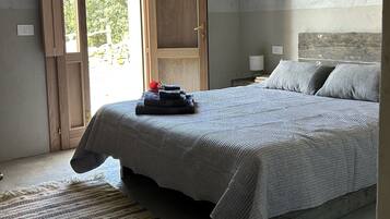 Une chambre à coucher avec un lit, une table de chevet, une porte en bois et une vue sur la verdure.