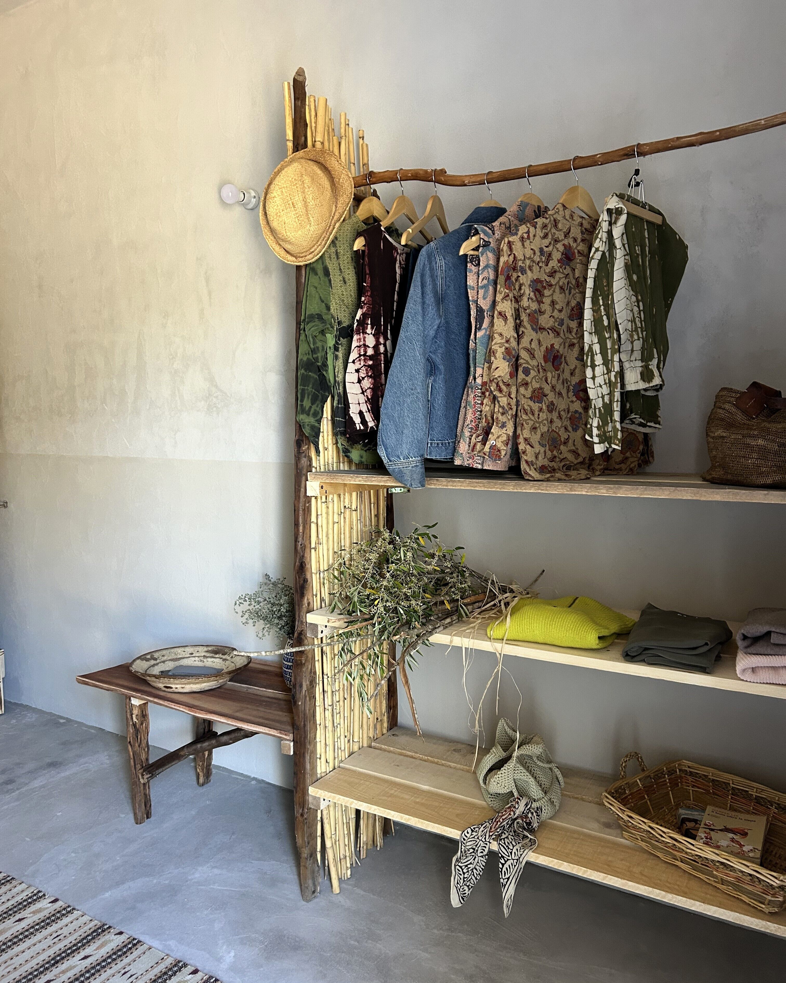 Een eenvoudige kamer met een houten plank waarop kleding, een hoed en een mandje liggen.