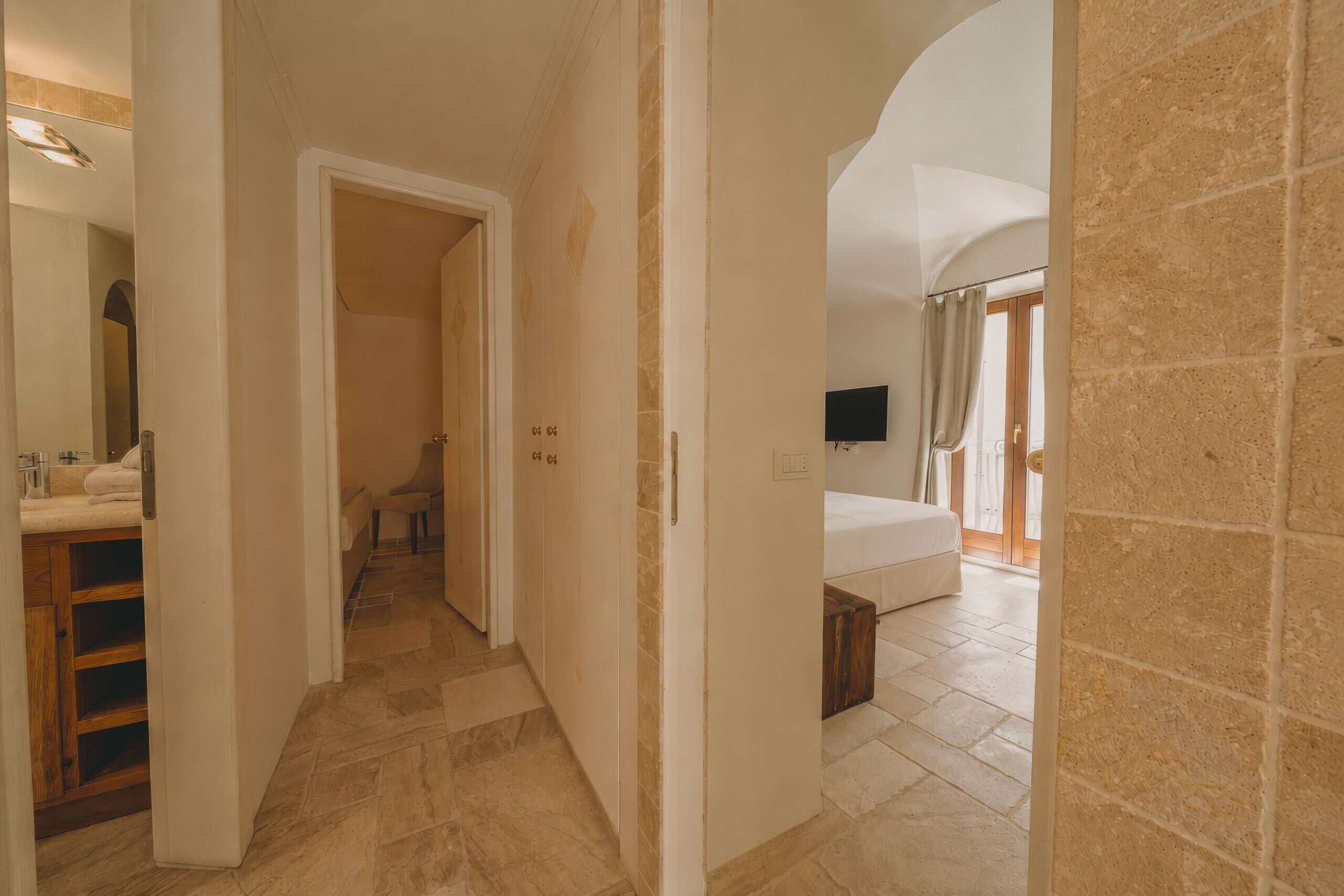 A hallway with a bathroom on the left, a bedroom with a TV on the right, and a staircase leading to another floor.