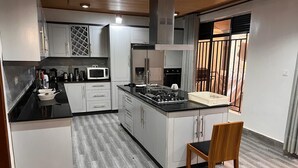 A modern kitchen with white cabinets, a black countertop, and a wooden chair. - 7-bedroom house in lovely Gacuriro for your stay (Kigali)