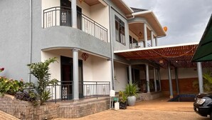 A two-story building with a balcony, a covered outdoor area, and a paved entrance. - 7-bedroom house in lovely Gacuriro for your stay (Kigali)