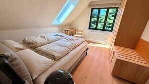 A bedroom with a bed, a small table, a chair, a radiator, and a window with a view of trees. - New: High-End Design Lodge Surrounded by Nature – Teos im Wiedergut (Sternberg)
