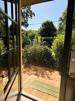 A view through a glass door into a garden with a paved area and a variety of plants. - New: High-End Design Lodge Surrounded by Nature – Teos im Wiedergut (Sternberg)
