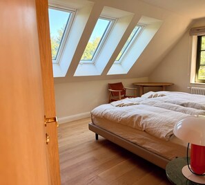 A bedroom with a sloped ceiling, skylights, a bed, a chair, a table, and a radiator. - New: High-End Design Lodge Surrounded by Nature – Teos im Wiedergut (Sternberg)