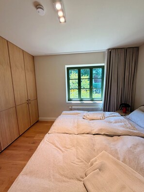 Un dormitorio con cama, ventana con vista a follaje, radiador y armario.