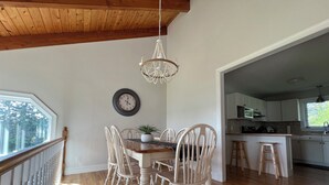 Un coin repas avec une table et des chaises en bois, un lustre, une horloge et une vue sur la cuisine.