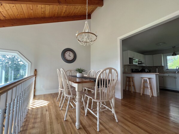 Zona pranzo con tavolo e sedie in legno, un lampadario, un orologio e vista sulla cucina.