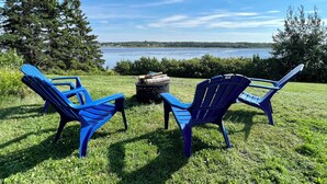 Deux chaises Adirondack bleues, placées face à un lac, avec une forêt en arrière-plan.