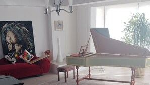 Una sala de estar con un piano de cola, un sofá rojo, un cuadro y un ventanal grande.