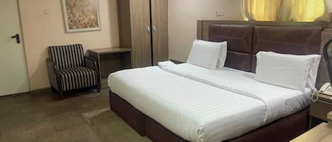 A hotel room with a large bed, a chair, a wardrobe, and an air conditioning unit.