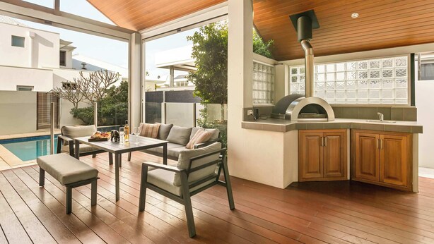 An outdoor kitchen area with a grill, wooden cabinets, and a dining set.