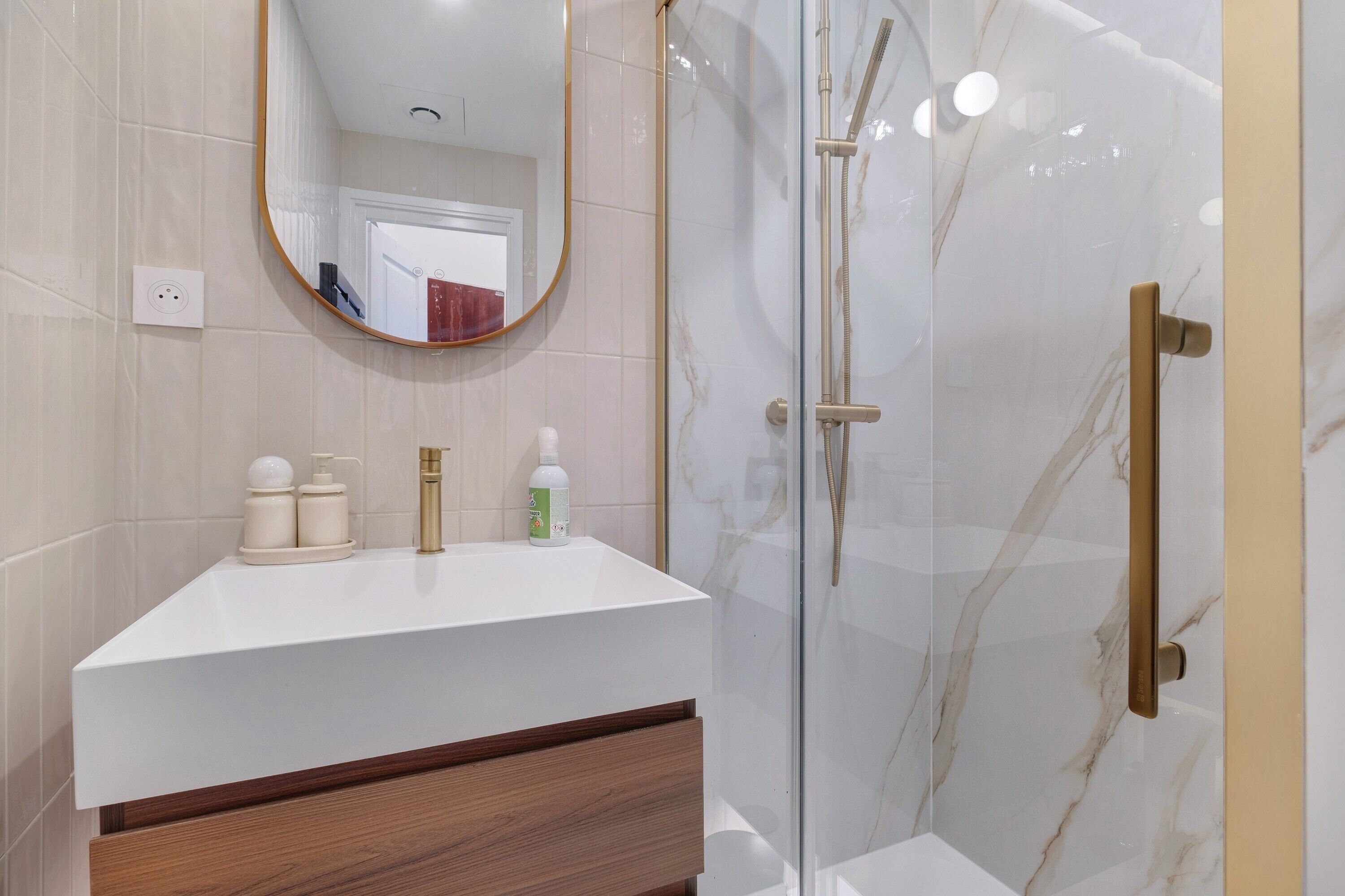 Une salle de bain avec un meuble-lavabo blanc, un miroir, une cabine de douche en verre et un mur recouvert de carreaux de marbre.