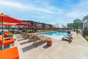 A poolside area with lounge chairs and umbrellas, a clear sky, and a building in the background.