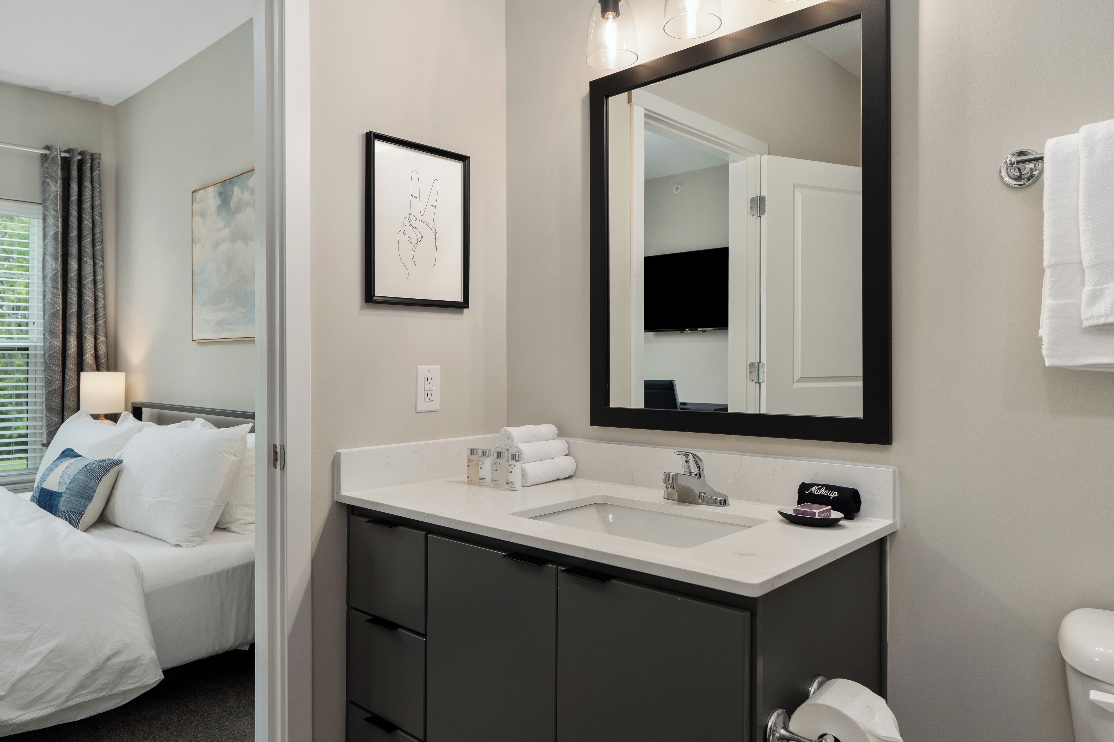 Habitación de hotel con cama, baño con un espejo grande, lavamanos e inodoro.