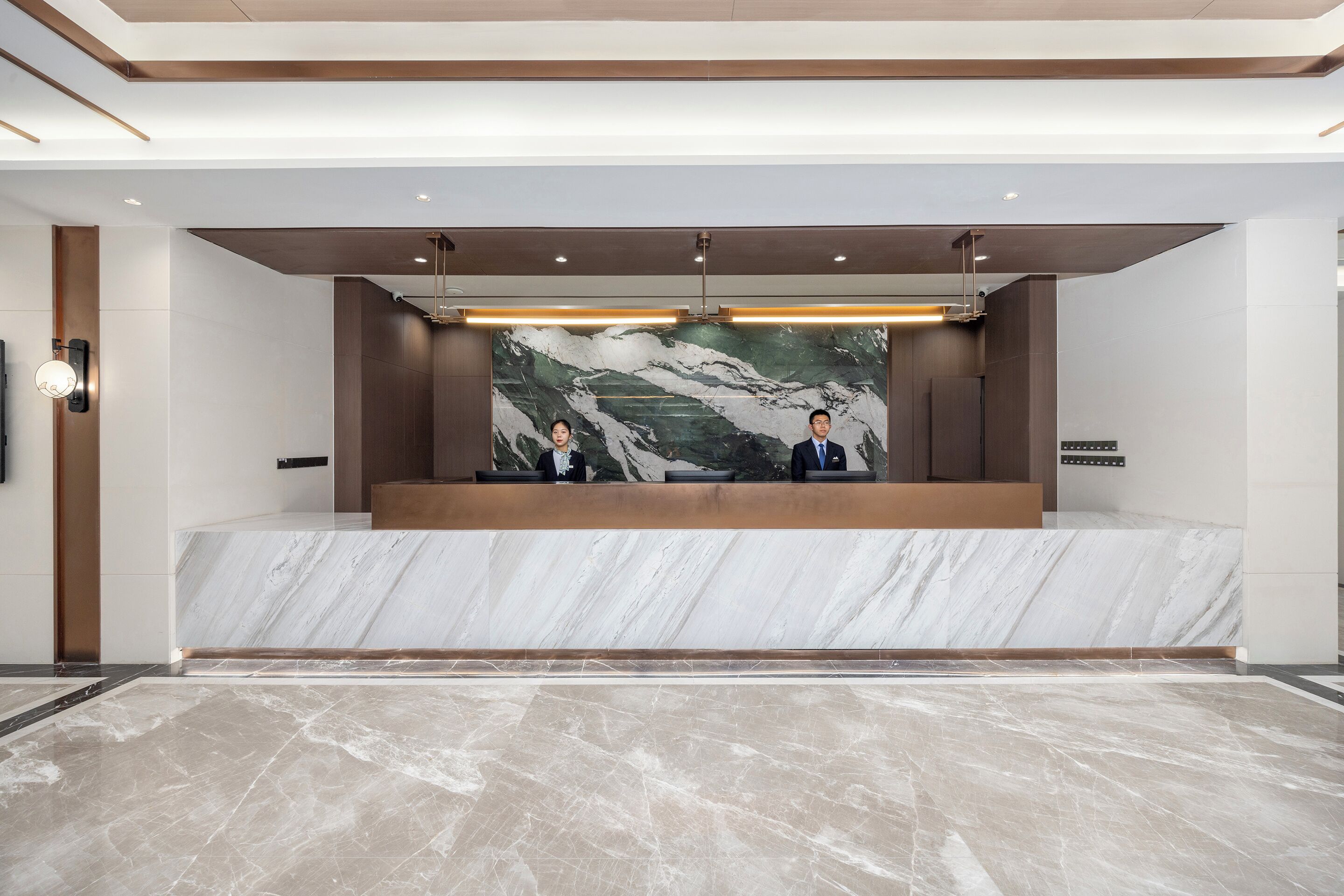 A reception area with a marble counter, two receptionists, and a large wall mural.