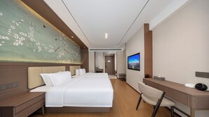 Habitación de hotel moderna con una cama grande, un escritorio, una silla, un televisor y una pared con un mural floral.