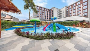 Piscina con toboganes y zona de juegos, rodeada por un edificio con múltiples ventanas y balcones.