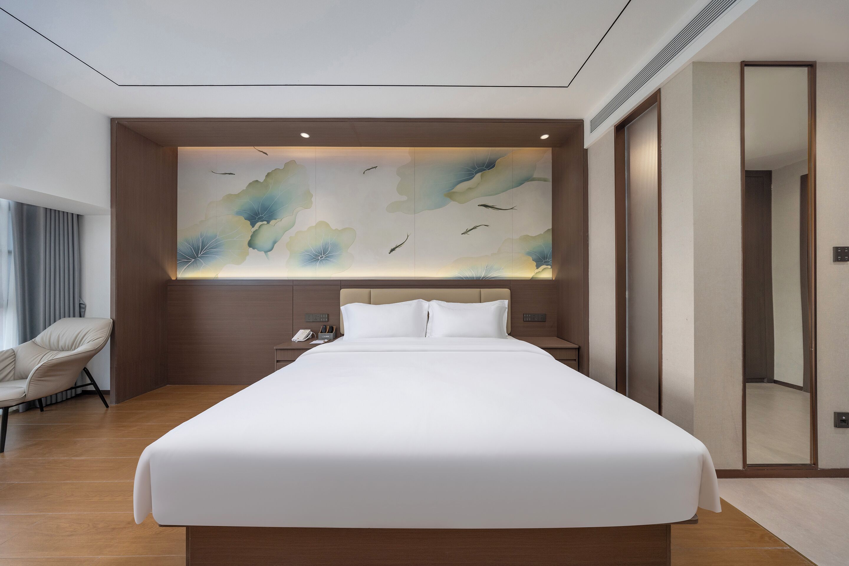 Habitació d'hotel moderna amb un llit gran, una zona de seients amb una cadira, una obra d'art penjada a la paret i un mirall.