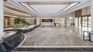 Un lobby amplio con piso de mármol, una recepción, una planta grande en maceta y una escalera al fondo.