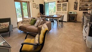 A spacious living area with a sofa, yellow armchair, dining table, and kitchen area with cabinets and appliances. - Arola Rustic Retreat (Arola-Preazzano)