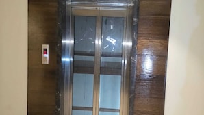 Un ascensor con pantalla digital, felpudo verde en la entrada y pared de mármol.
