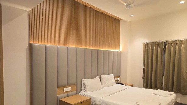 Habitación de hotel moderna con una cama grande, una mesita de noche, un panel de pared de madera y un ventilador de techo.