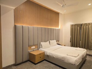 A modern hotel room with a large bed, a nightstand, a wooden panel wall, and a ceiling fan. - Sai Madhura A Luxury Hotel  (Hyderabad)