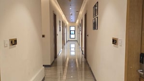 Un largo pasillo bien iluminado, con suelo de mármol, puertas a ambos lados y una vista despejada hasta el final.
