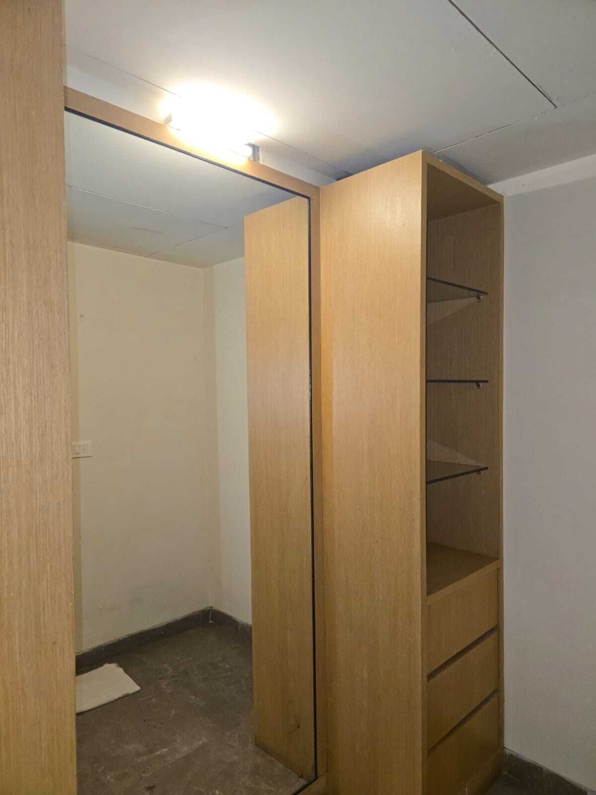 Un armario de madera con varios estantes, una lámpara en el techo y una puerta visible solo en parte.