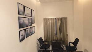 Un salón de conferencias con ventilador de techo, una mesa con cuatro sillas y una fila de cuadros en la pared.