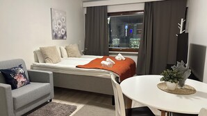 Ett modernt hotellrum med en säng, en grå soffa, ett matbord och ett fönster med gardiner.
