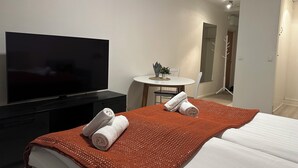 Ett hotellrum med en säng, en tv, ett litet runt bord med en växt och en dörr som leder till ett badrum.