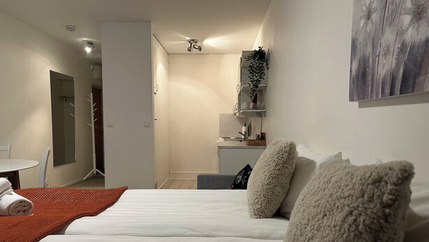 Ett hotellrum med en säng, ett litet bord med en stol, ett litet kök och ett badrum.