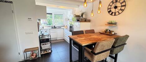 A modern kitchen with a dining area, featuring a wooden table, black chairs, and pendant lighting.