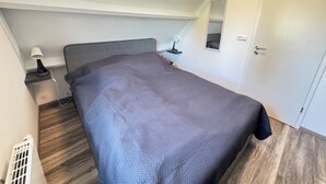 Ein Schlafzimmer mit Bett, Nachttisch, Lampe und Tür.