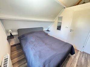 A bedroom with a bed, bedside table, lamp, and a door. - Het Baken 163, a quiet resort near Lake Grevelingen and the North Sea (Scharendijke)