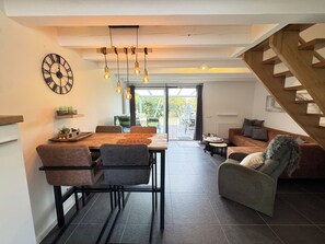 A modern interior with a dining area, a sofa, a staircase, and a view through a glass door. - Het Baken 163, a quiet resort near Lake Grevelingen and the North Sea (Scharendijke)