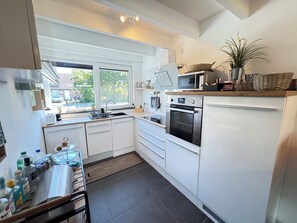 A modern kitchen with white cabinetry, a built-in oven, a microwave, and a window providing a view of the outside. - Het Baken 163, a quiet resort near Lake Grevelingen and the North Sea (Scharendijke)