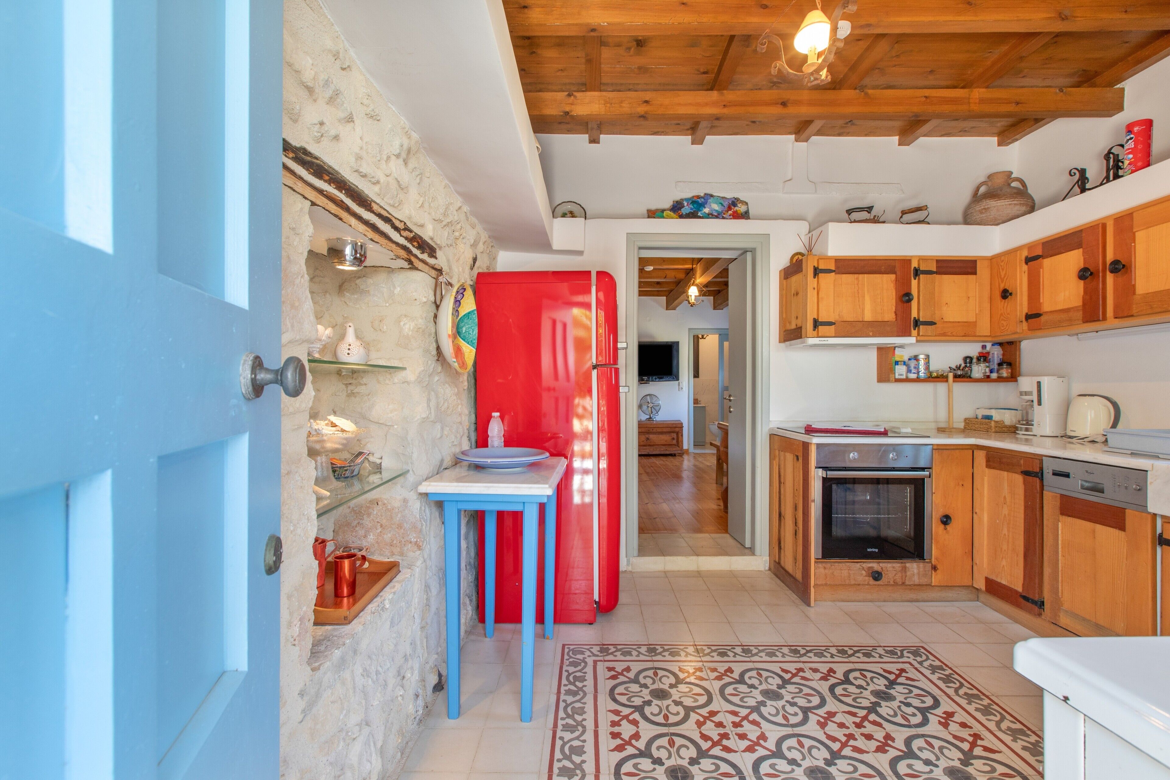 A kitchen with wooden cabinets, a red refrigerator, and a blue table.