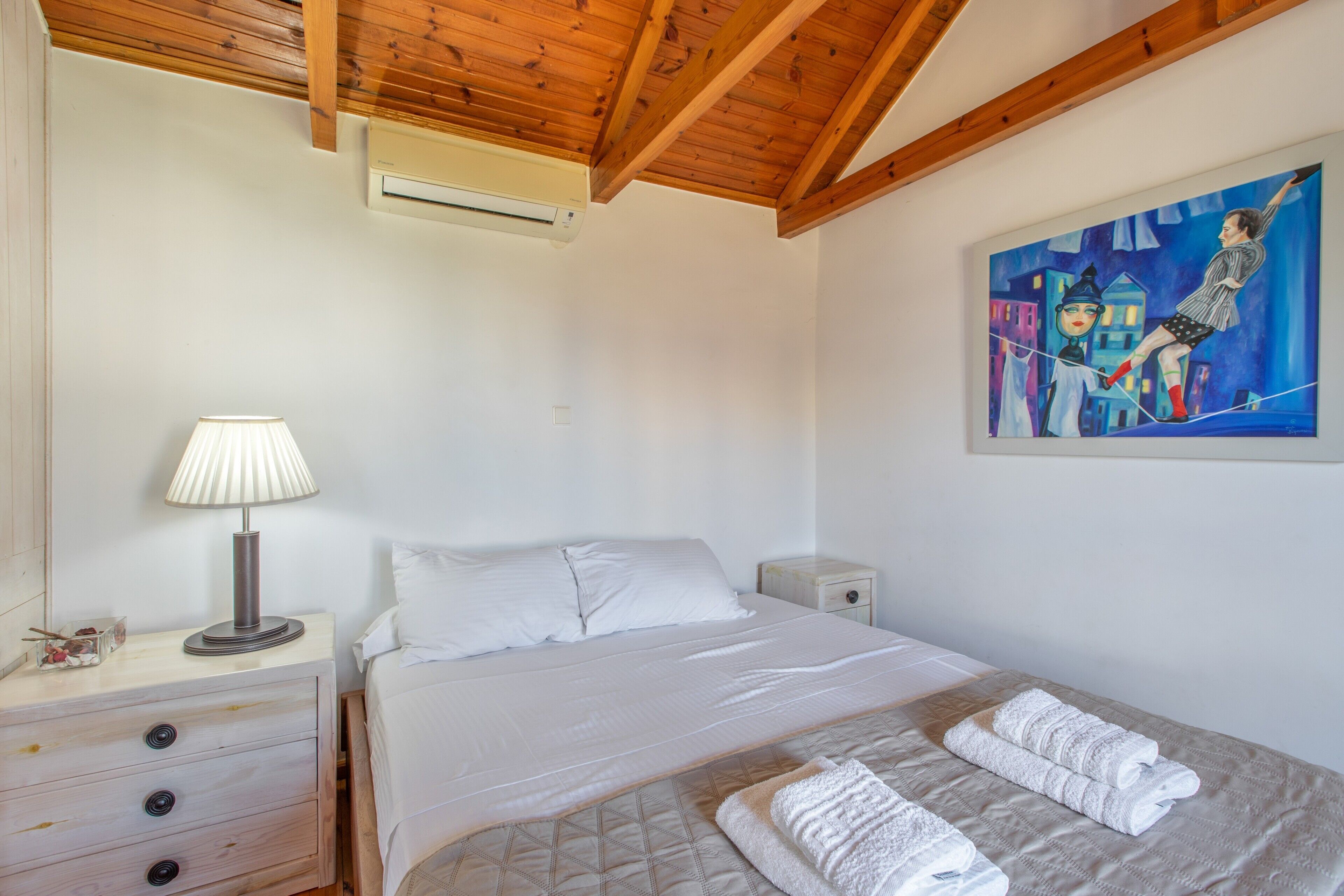 Una camera da letto con un letto, un comodino, una lampada, un quadro appeso al muro e un soffitto in legno.