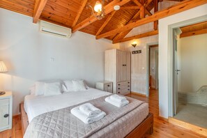 Un dormitorio con techo de madera, una cama con ropa blanca, una mesita de noche, un armario y una puerta que da a otra habitación.