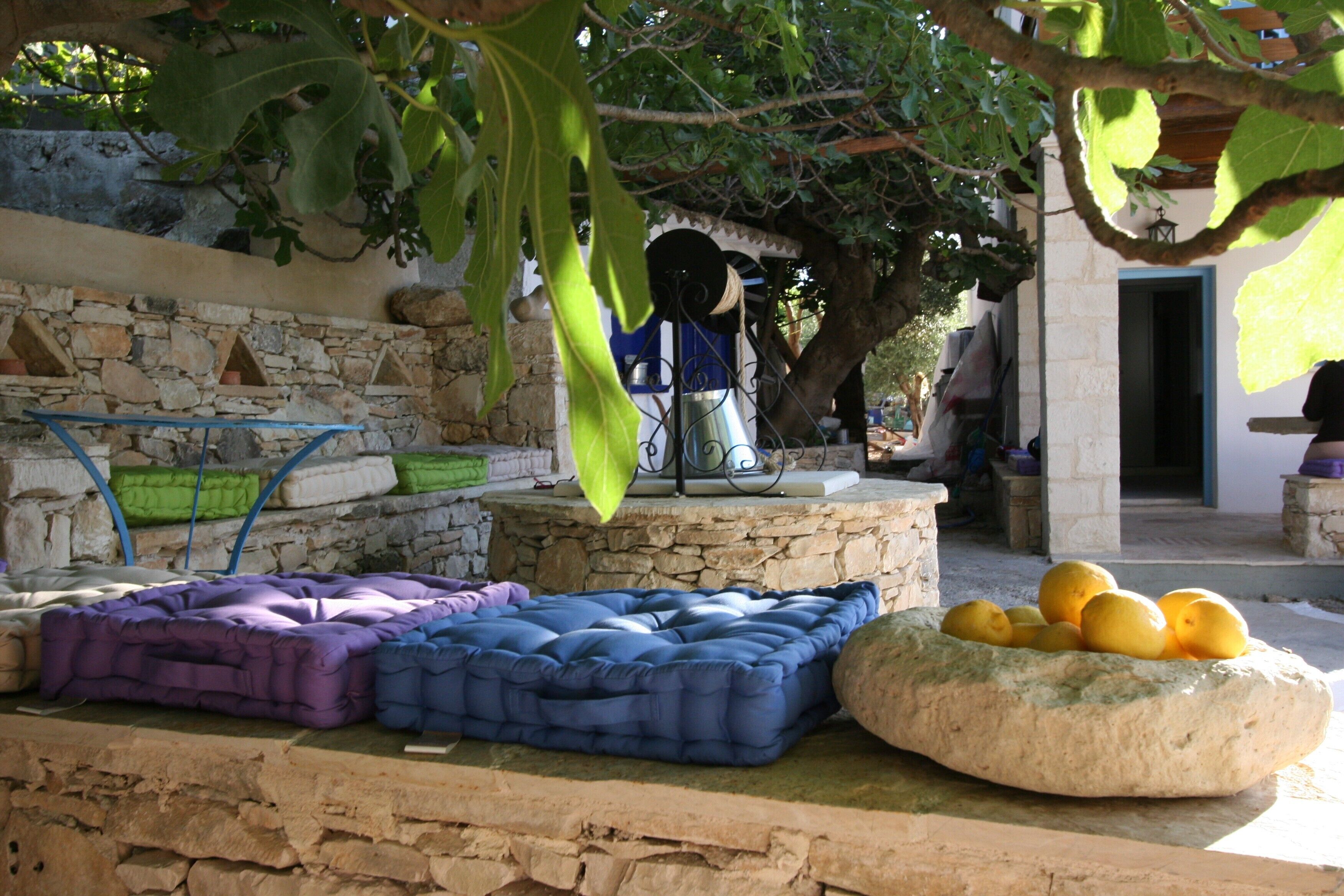 A stone wall with a stone bench, a metal table with a blue cloth, and a basket of lemons.