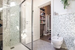 Een badkamer met een douchecabine van glas, een wit wastafelmeubel en een betegelde spatwand.