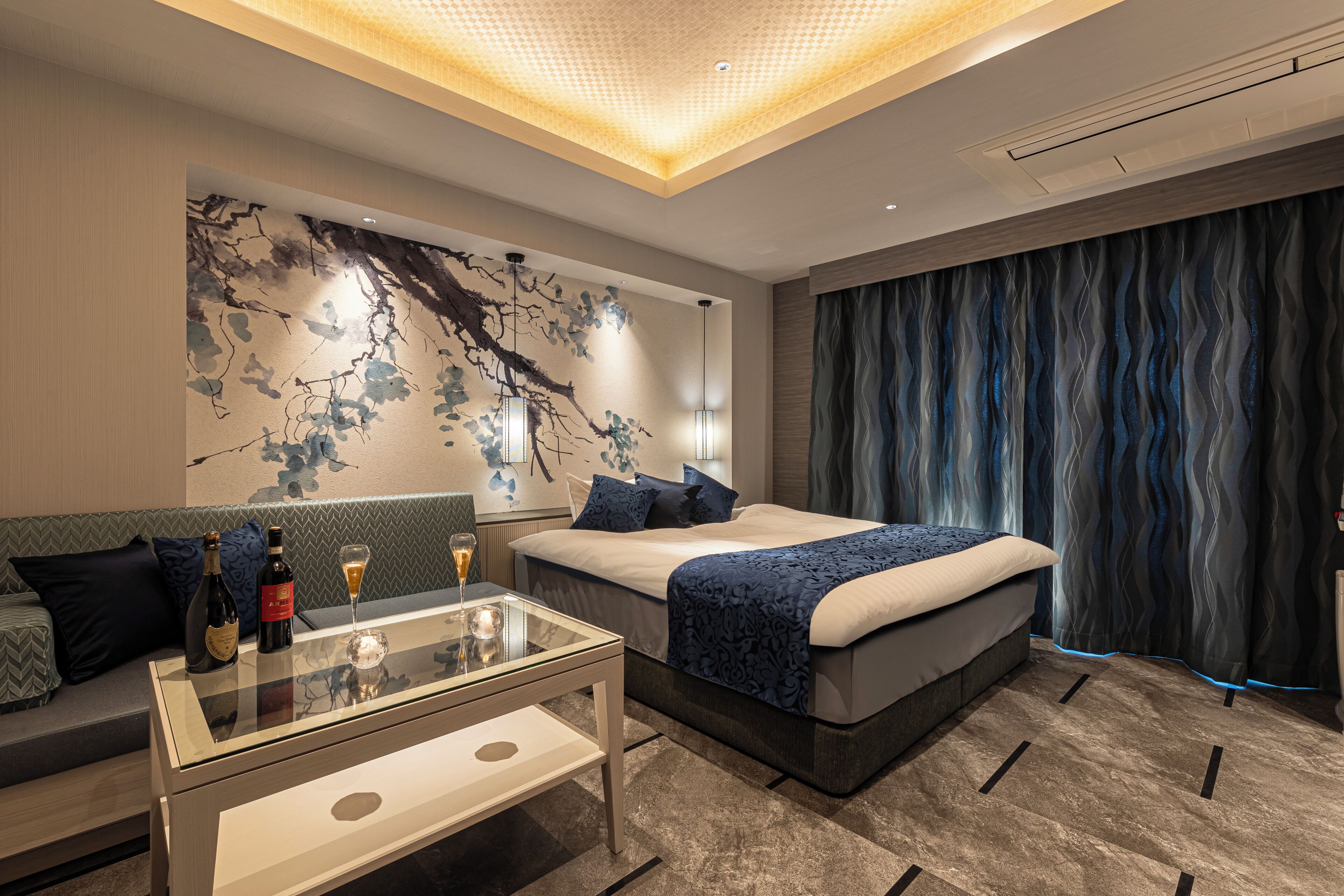 Una habitación de hotel moderna con una cama, una mesa de centro de vidrio, un sofá y una pared con un mural decorativo.