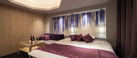 A modern hotel room with a large bed, a small table with drinks, and a decorative wall.