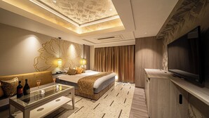 A modern hotel room with a bed, sofa, TV, and a glass coffee table.