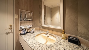 A bathroom with a granite countertop, a sink, a mirror, and a shelf with toiletries.